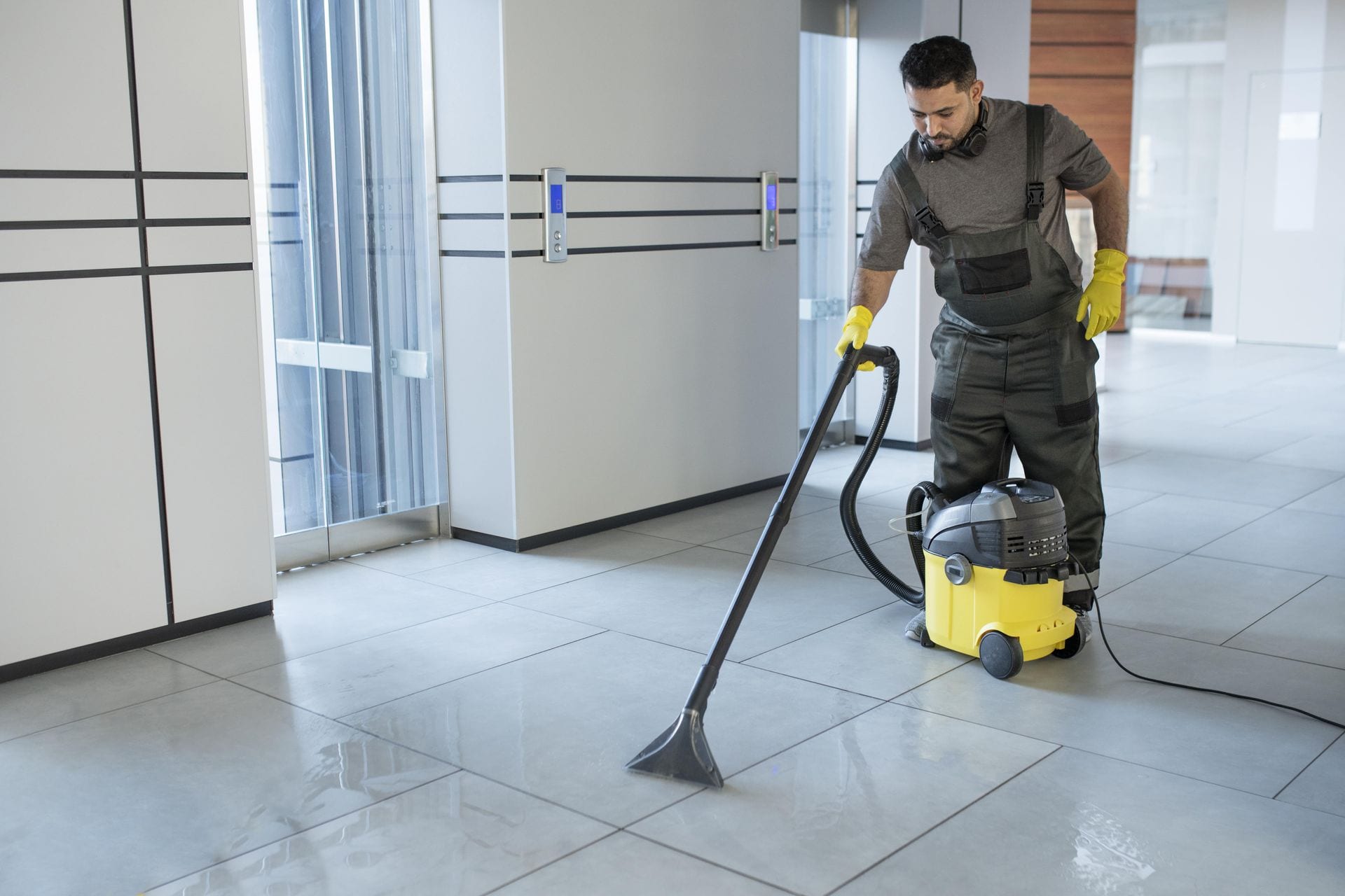 Worker using a vacuum cleaner to clean a tiled office floor