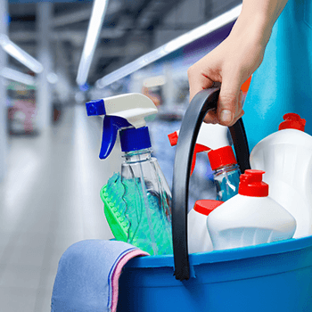 Hand holding a blue cleaning caddy with spray bottle and cleaning supplies in a store aisle