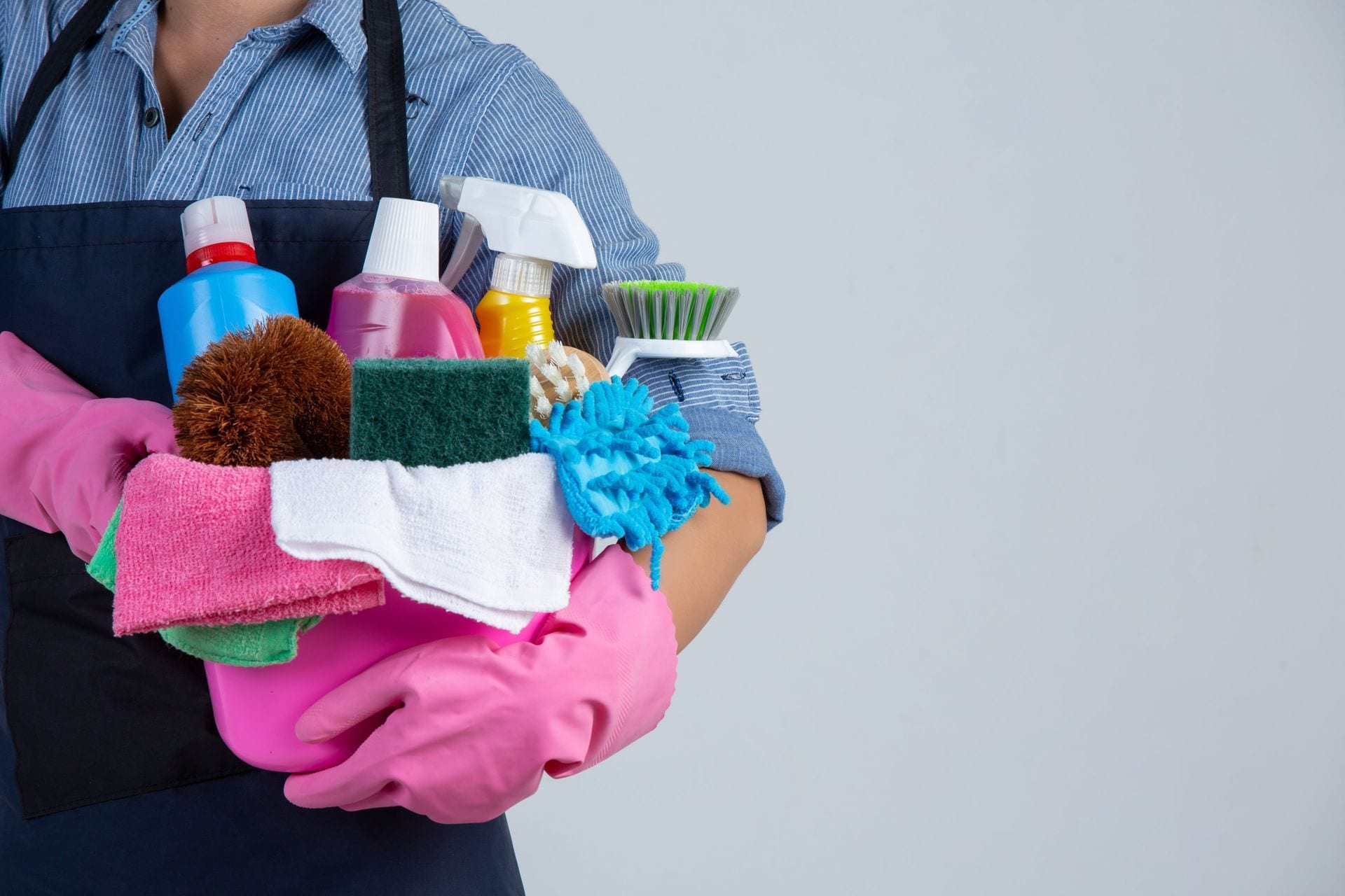 Person holding cleaning supplies and cloths, wearing pink gloves and apron